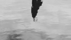 imatge en blanc i negre d'una superficie d'aigua on s'intueix el reflex d'una persona.